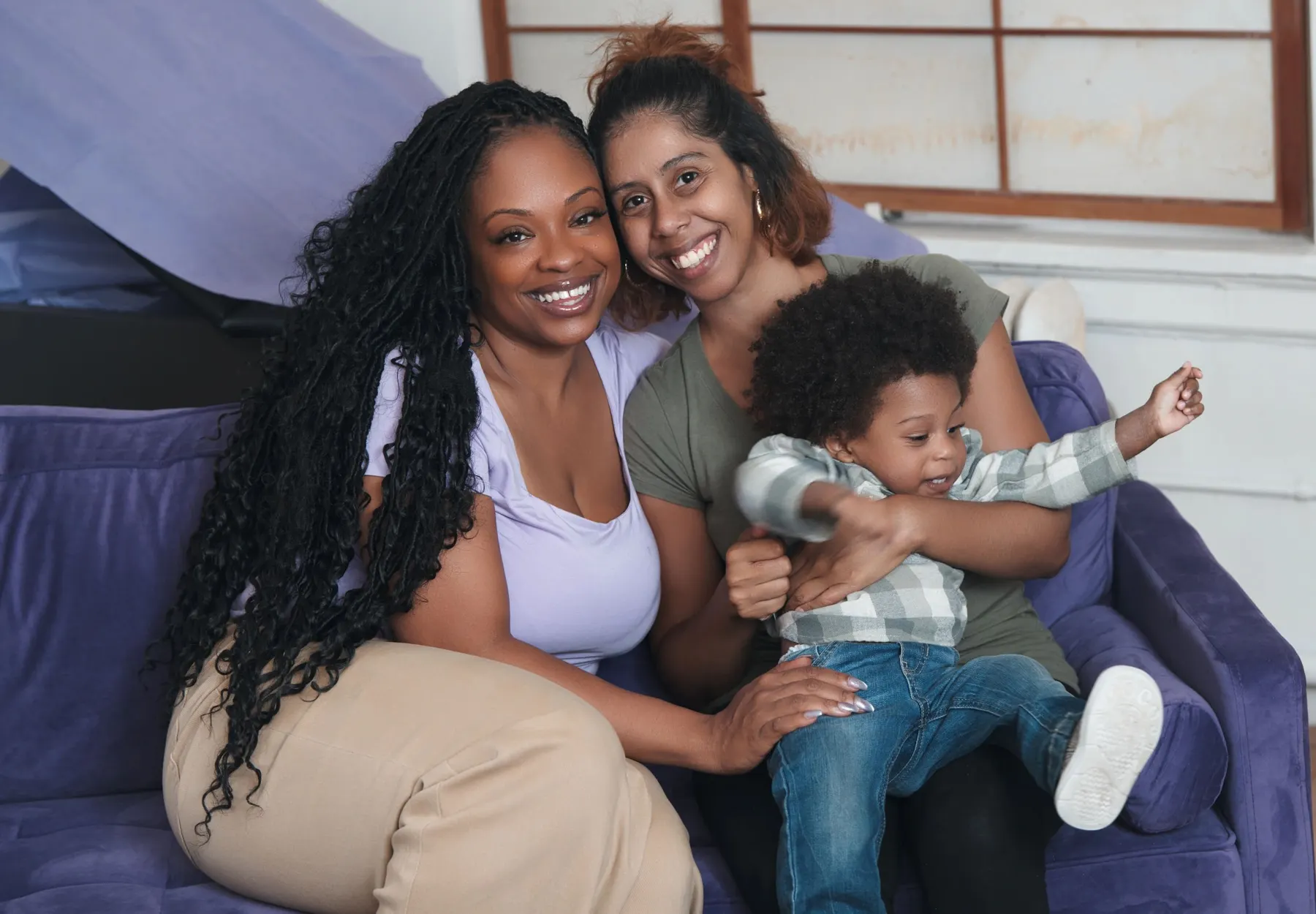 Three generations of women laughing together on a sofa with a toddler